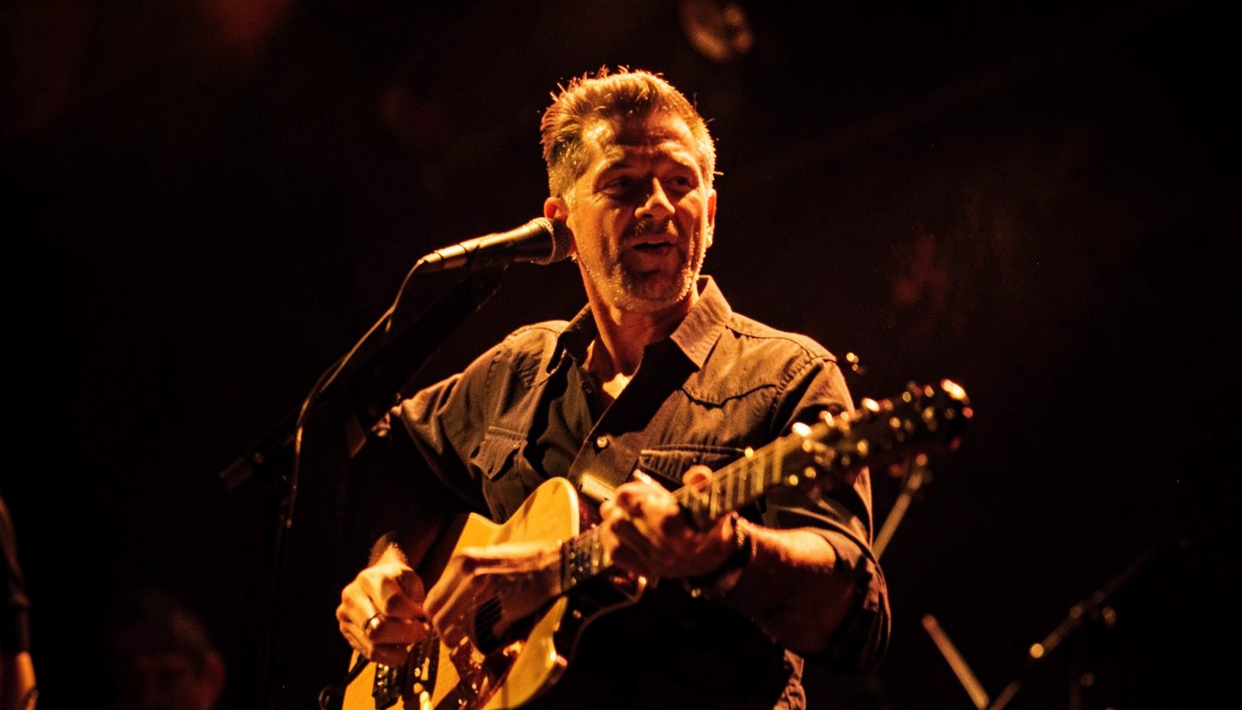Close-up musical performance frame with rich amber stage lighting and dark background