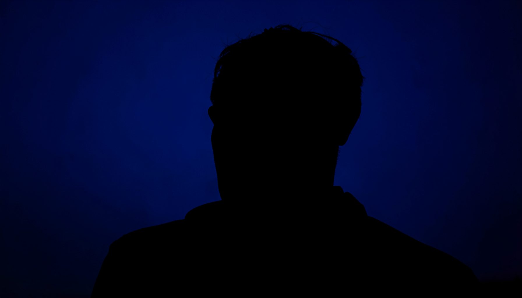 Dramatic silhouette shot with deep indigo background and subtle rim lighting