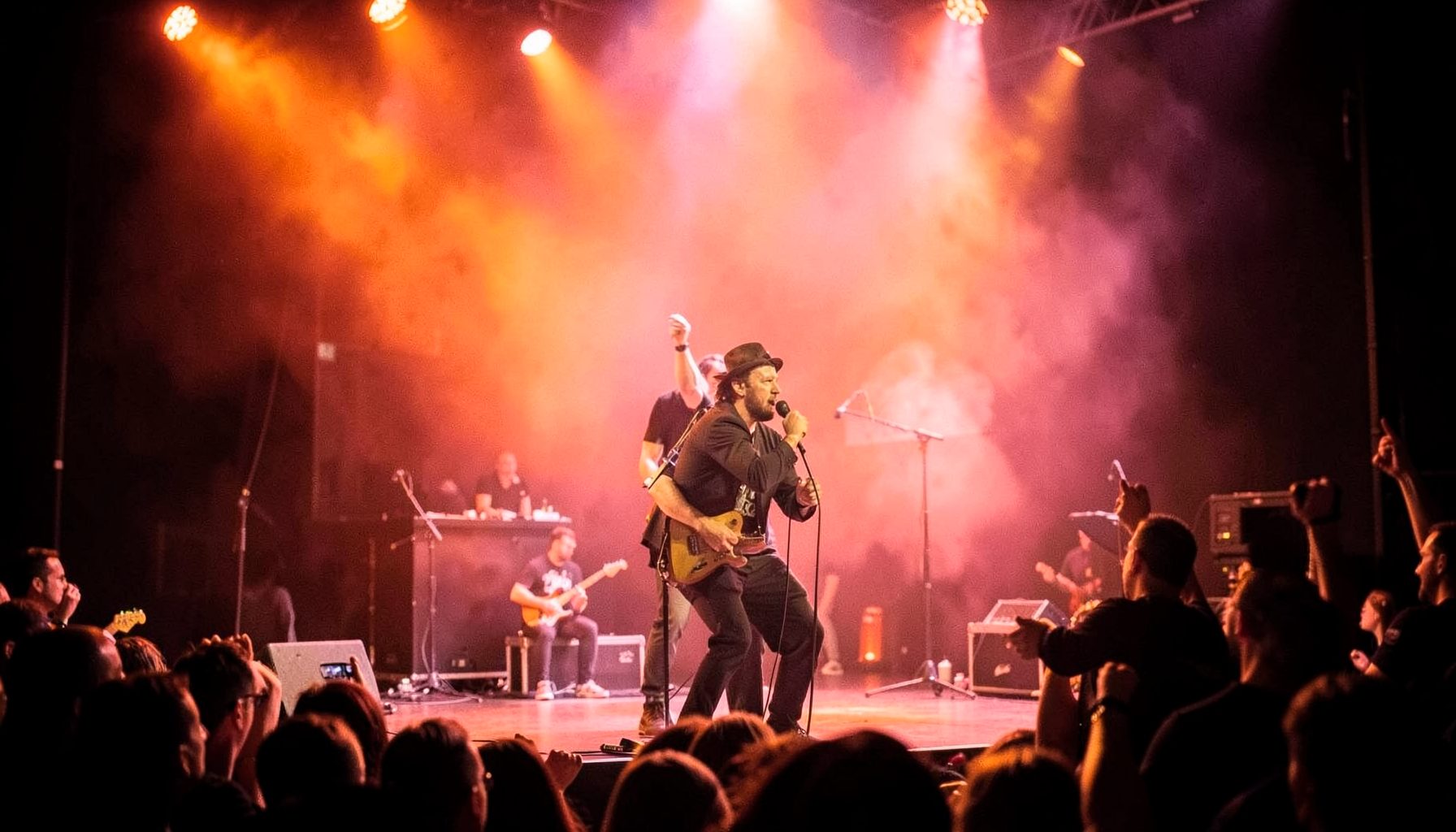 Bright stage-lit performance still with warm orange and pink hues, capturing a live rendition