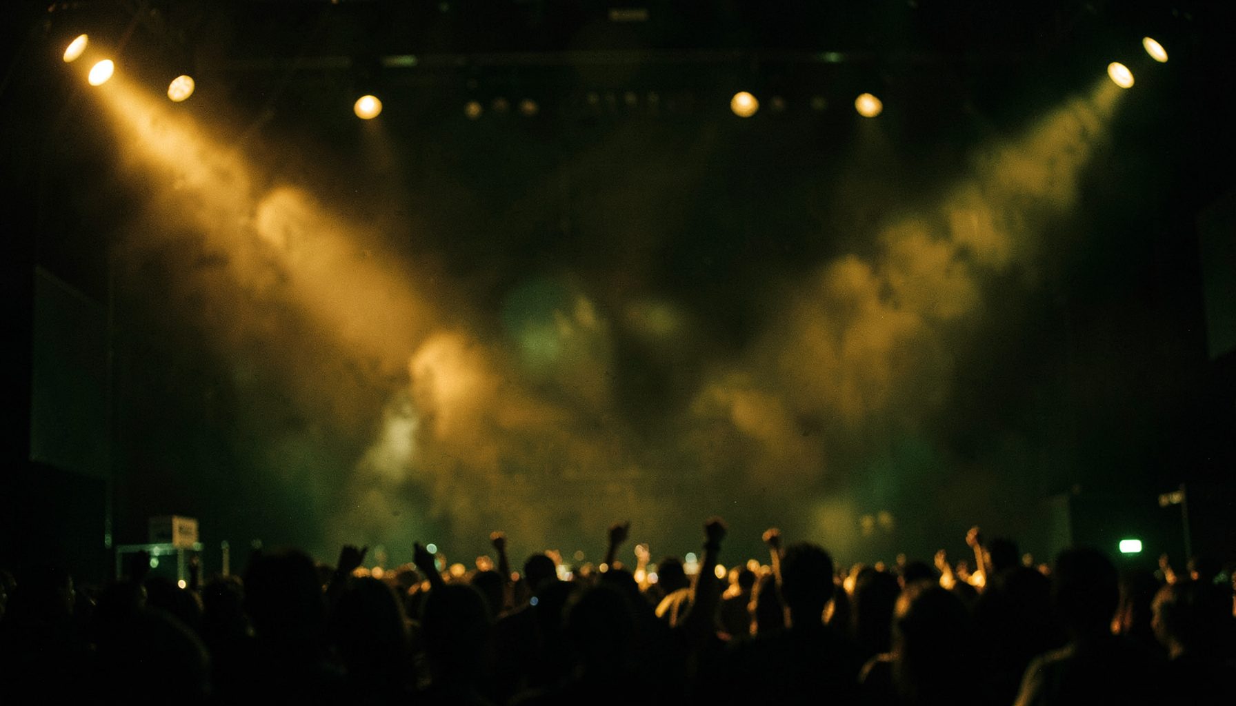 Warm amber and gold stage lights with soft bokeh, a moody concert atmosphere in deep greens and blacks